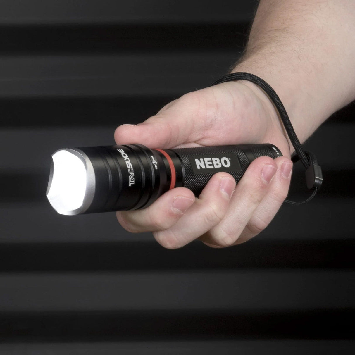 Handheld flashlight labeled ’NEBO’ being gripped by a person’s hand.
