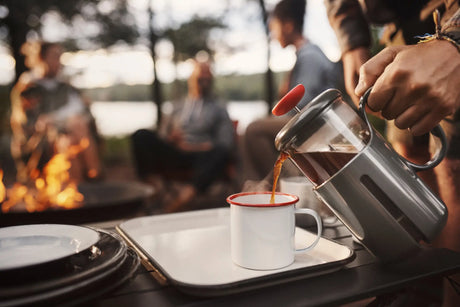 Coffee being poured from a percolator into a white enamel mug.