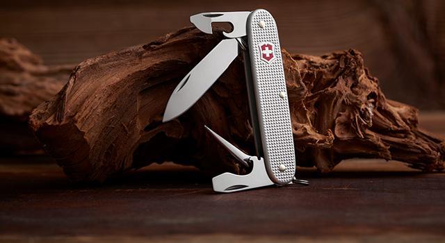 Swiss Army knife with an open blade resting against a piece of wood.