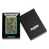 Zippo lighter with an intricate green and white design on its face, displayed next to its black packaging box.