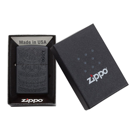 Zippo lighter with an intricate skull design engraved on its surface, displayed in its packaging.