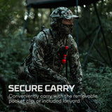 Camouflaged soldier in tactical gear holding a weapon in a forest setting.