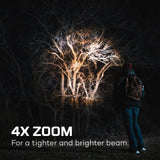 Person illuminating bare trees at night with a bright flashlight or spotlight.