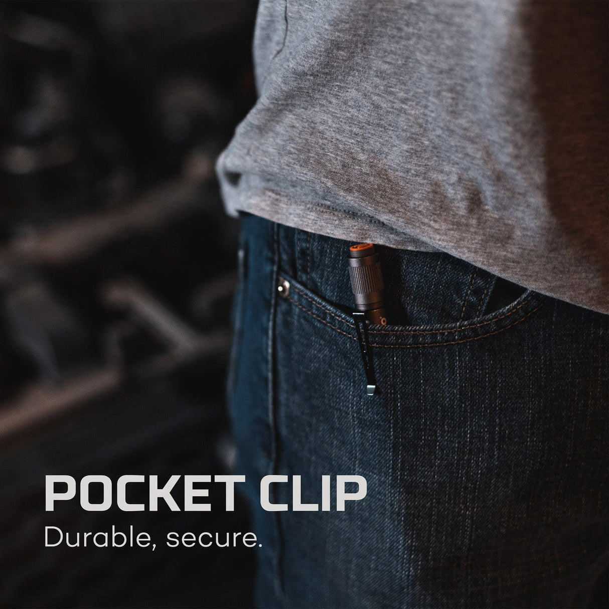 Pocket clip attached to a pair of jeans, partially visible beneath a gray shirt hem.