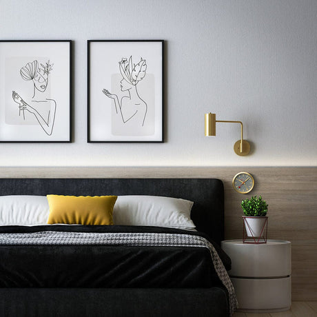 Modern bedroom with a black bed, minimalist artwork, and gold wall sconce.