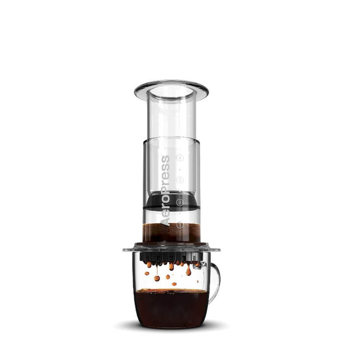 Aeropress coffee maker with a clear chamber and dark coffee dripping into a glass mug below.