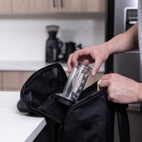 Hands placing a reusable water bottle into a black bag.