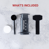 Cylindrical coffee press labeled ’AeroPress’ with accompanying accessories.