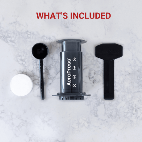 Cylindrical coffee press labeled ’AeroPress’ with accompanying accessories.