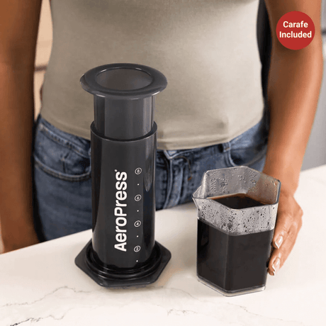 AeroPress coffee maker with a cup of brewed coffee beside it.